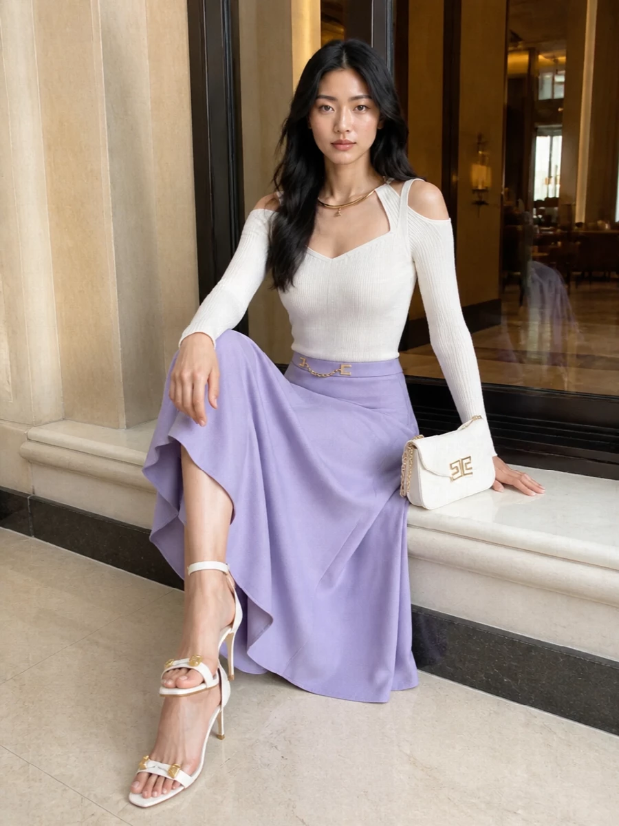 A softly sculpted ivory knit skims into the lavender midi, keeping the focus on a cinched, gold-framed waist and the skirt’s fluid movement. White and off-white accessories, all touched with gold, keep the palette calm and luminous for polished daytime events or early evening drinks.