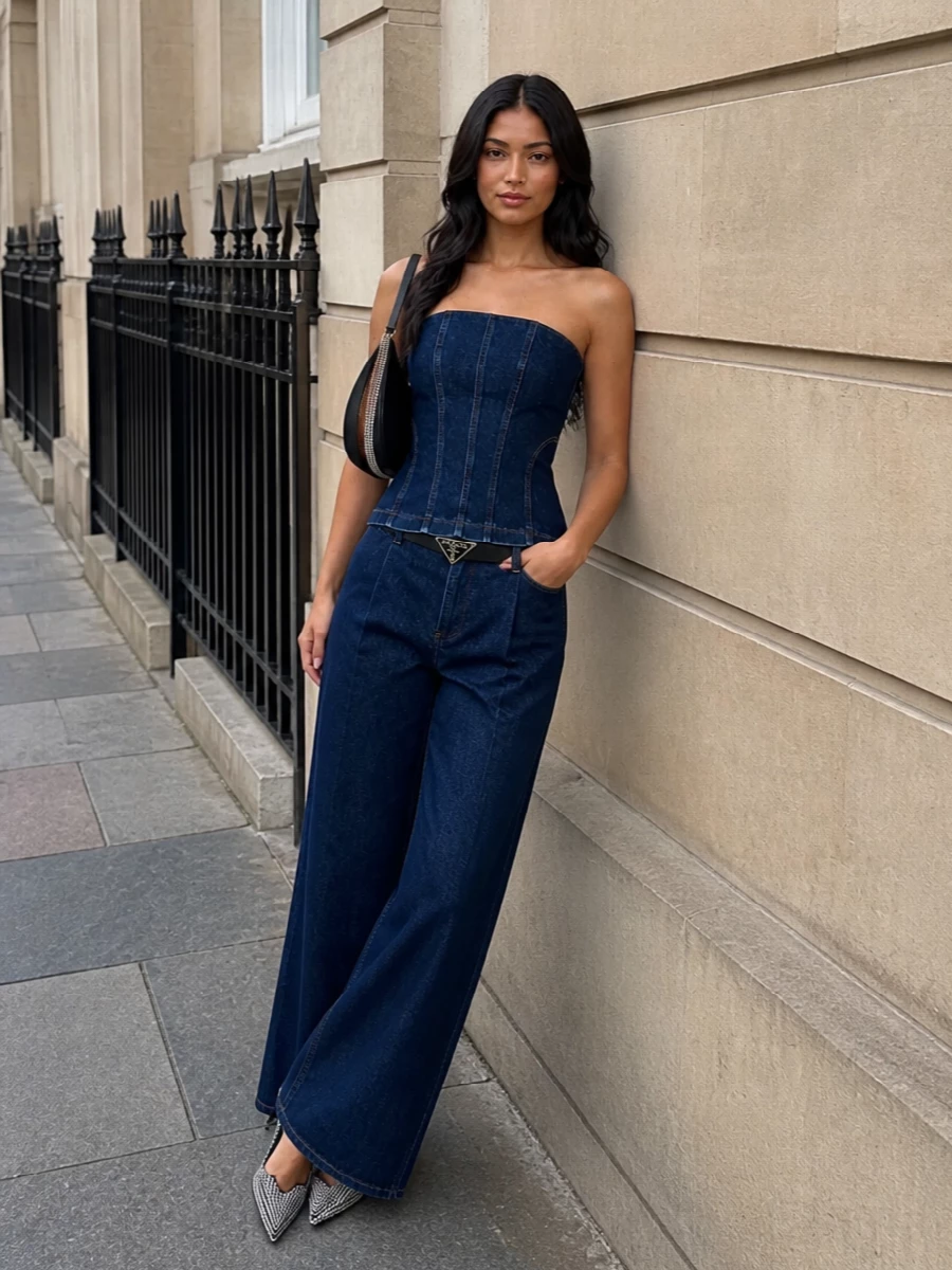 Dark indigo denim is treated almost like tailoring here, with the sculpted corset and matching wide leg working as a clean, elongated column for night. A pointed crystal slingback and a black crescent shoulder bag introduce just enough metal and shine to keep it firmly in the after‑dark territory while preserving the minimal, architectural mood. The slim logo belt is the only interruption at the waist, a subtle graphic line that frames the hourglass without cluttering it.