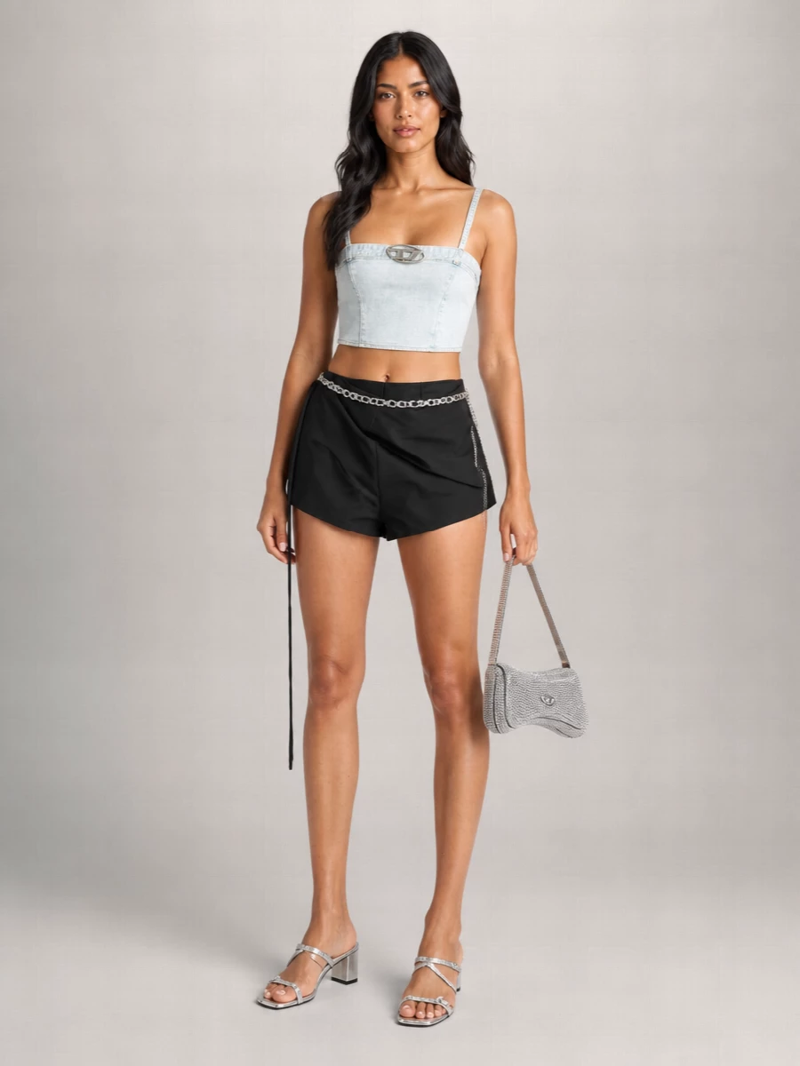 A cropped light-wash bustier meets sharp black wrap shorts for a leggy, club-ready take on early-2000s denim. Silver strappy sandals, a crystal micro bag and a slung chain belt pull the hardware story together, keeping the palette tight and the attitude unapologetically night-out. It is streamlined, high-summer and built to move from bar to dance floor without losing polish.