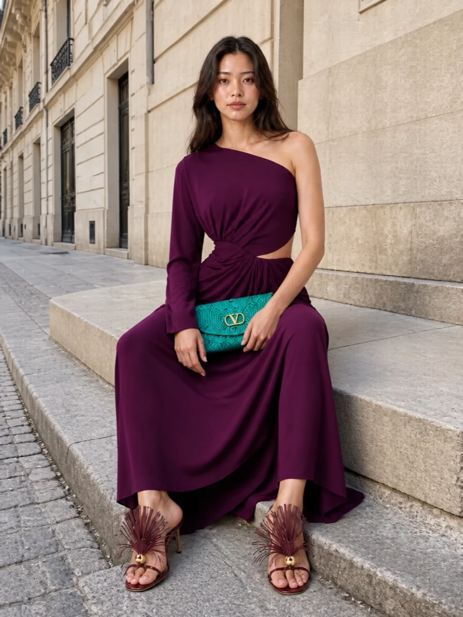 A sweep of deep plum jersey wraps the body in asymmetric draping, setting a moody, romantic backdrop for the turquoise floral Valentino clutch. Burgundy fringe-trim sandals keep the line light and sculptural, tying into the jewel-tone story without stealing focus. This path leans into a statuesque gown rather than separates, which best balances the clutch’s drama while preserving a clean, elongated evening silhouette.