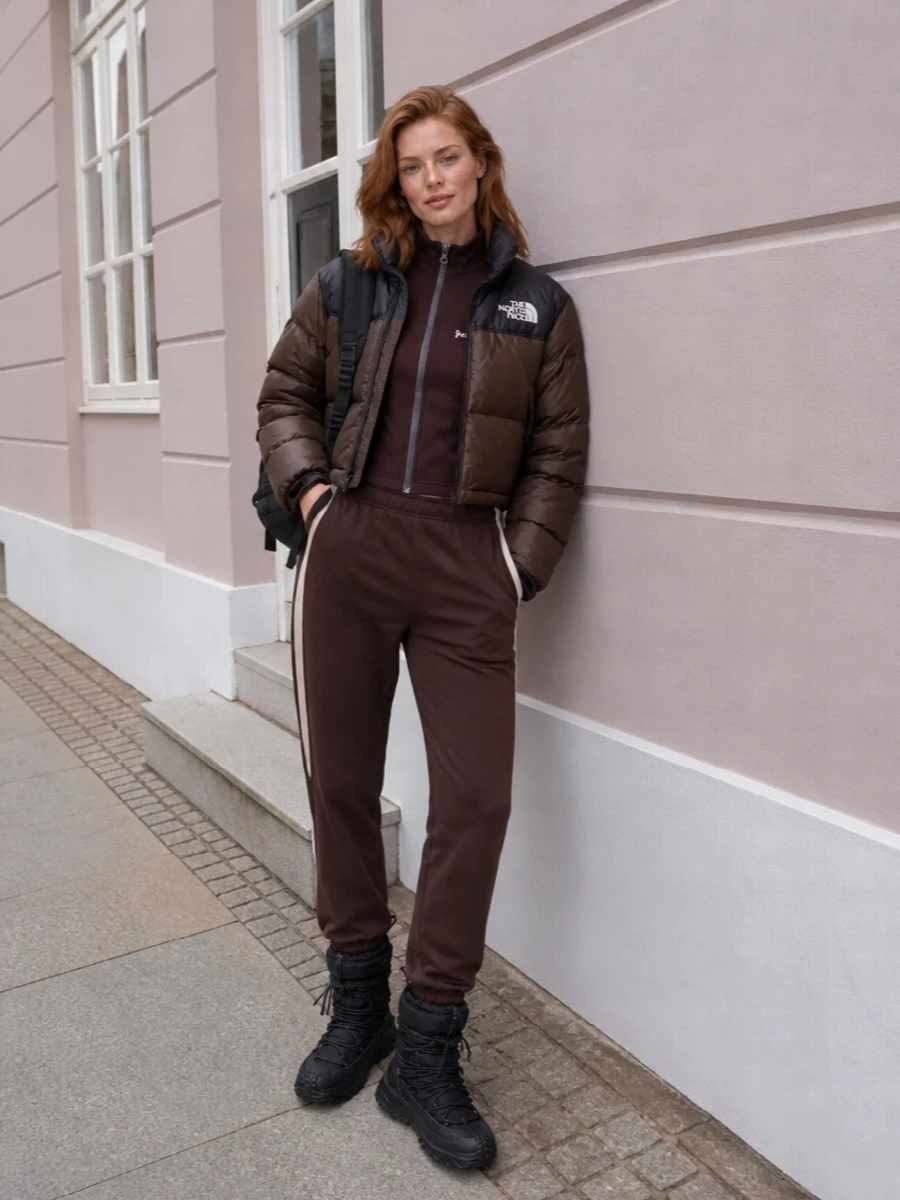I’m building this around a tonal brown and black city-outdoor story, so I’m skipping the dresses and leaning into a cropped-top-plus-track-pant base that really works with the puffer. The Palm Angels zip top mirrors the jacket’s sporty lines, the brown Canada Goose pant grounds everything without breaking the palette, and Moncler boots with a clean North Face backpack keep the mix performance-driven but still fashion-aware for cold city days and weekend escapes.