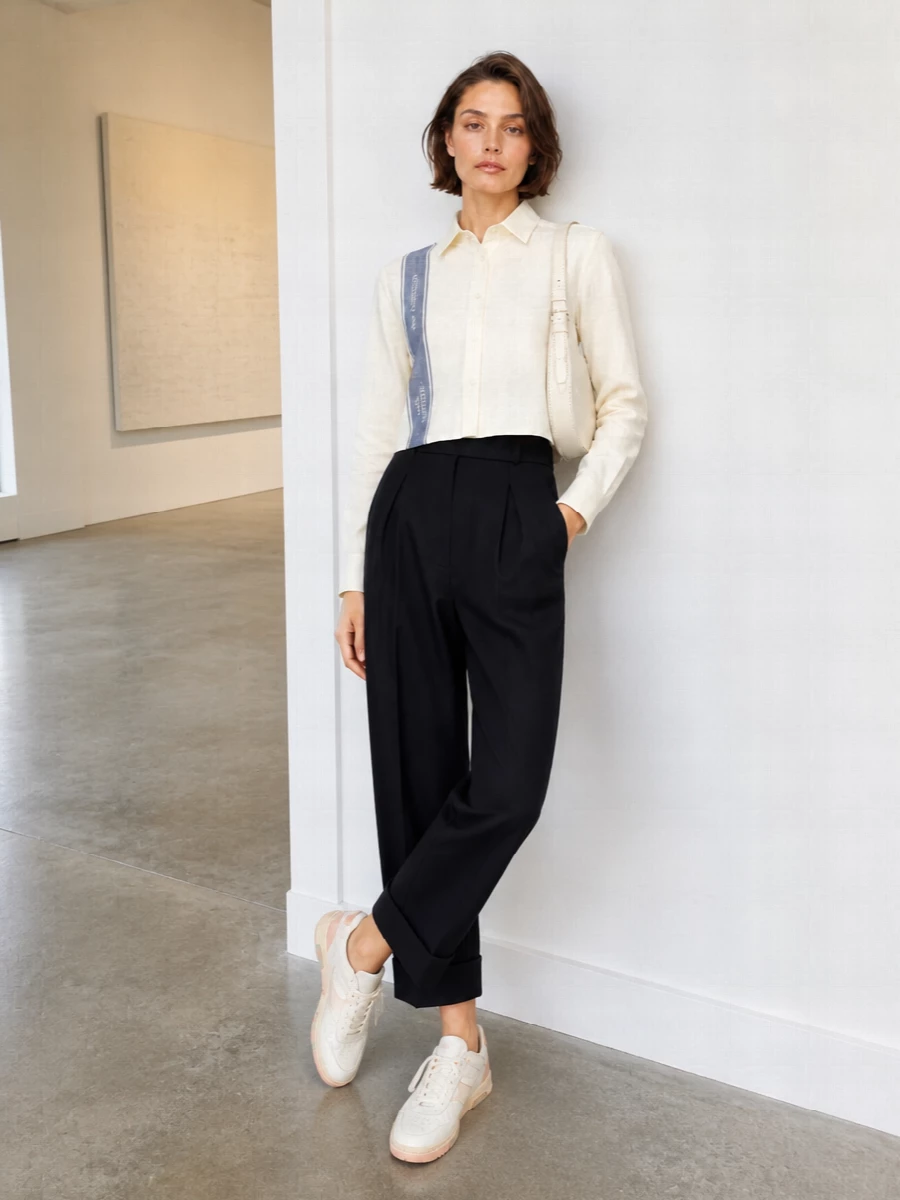 A cropped, logo-striped shirt meets high-rise inky tailoring for a summer outfit that feels sharp but not stiff. The voluminous cuffed trouser balances the shorter top, while creamy sneakers and a sculpted ivory cross-body keep the palette soft and considered. It is polished enough for city days yet relaxed enough to move easily from desk through late afternoon plans.