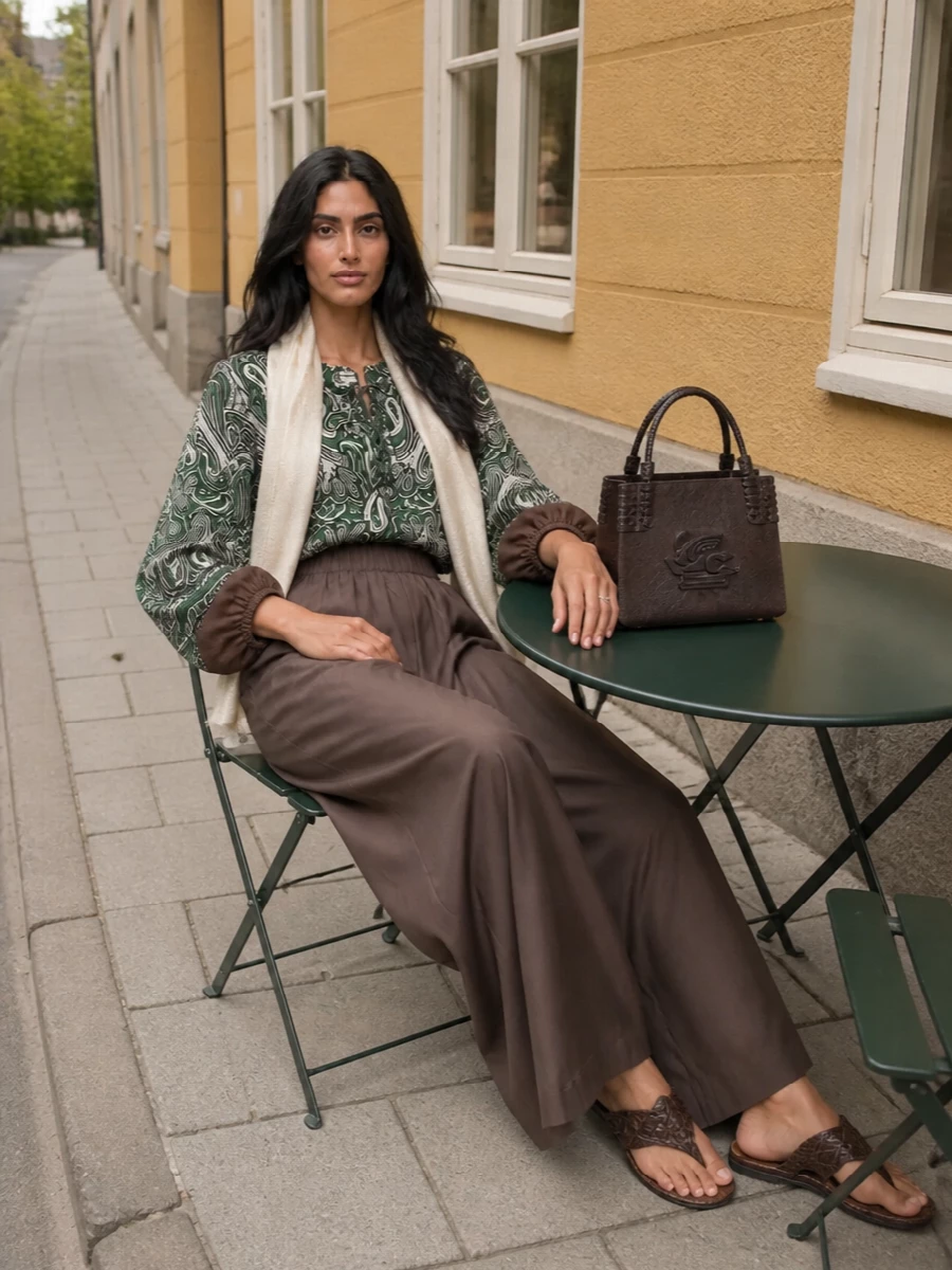 Emerald paisley and mocha brown meet in a relaxed, elongated silhouette that feels romantic yet grounded. The fluid blouse and wide-leg trouser keep the line easy, while braided leather sandals and a structured mini tote bring just enough polish. Soft neutrals at the neck warm the palette and let the blouse remain the quiet statement.