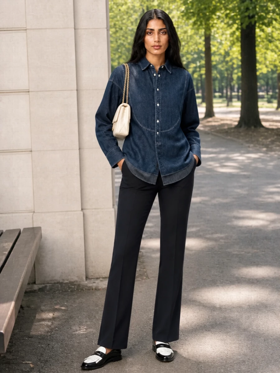 A dark indigo bib-front shirt is grounded with precise navy tailoring for a clean, quietly polished take on denim in the city. Patent mule loafers keep the line sharp without feeling stiff, while a cream quilted shoulder bag lightens the palette and nods to classic handbag codes. The result is relaxed office ready, equally at ease for weekend gallery visits or an unhurried lunch meeting.