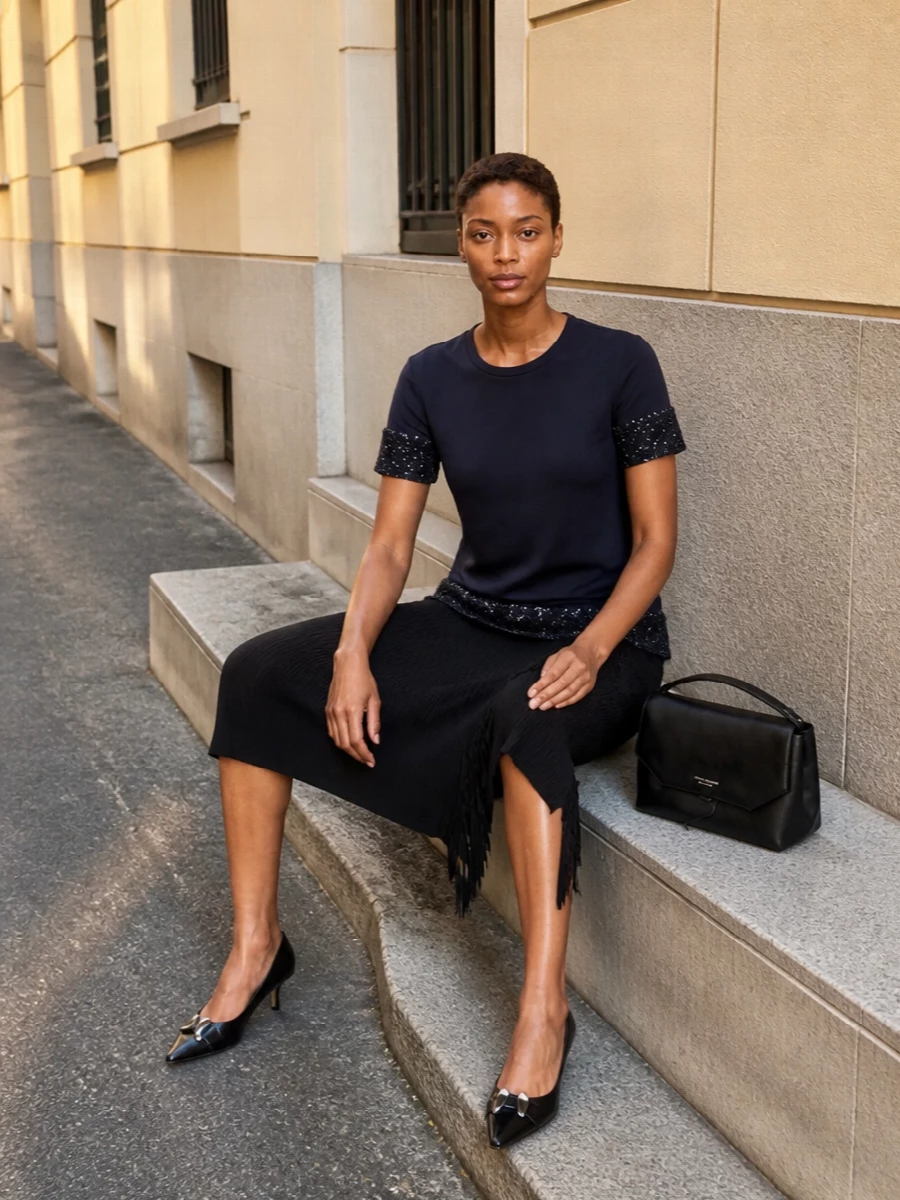 An inky sequinned tunic falls over a slim black ribbed midi, creating a clean vertical line that feels quietly glamorous rather than loud. A pointed black kitten heel and structured top-handle bag keep everything sharp and city-ready, while the softly sparkling scarf adds a final whisper of night-sky shimmer. It is an easy cocktail ensemble that moves from bar to late dinner with zero fuss but plenty of presence.