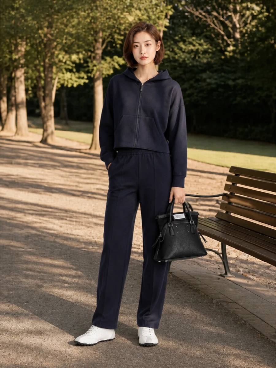 Ink track pants with a cropped navy hoodie create a low-contrast column that feels calm, athletic and considered. Margiela’s chalky retro runners keep it light at the base while the structured black tote adds just enough sharpness. The result is an easy city uniform that reads modern sport with a quiet edge rather than full logo drama.