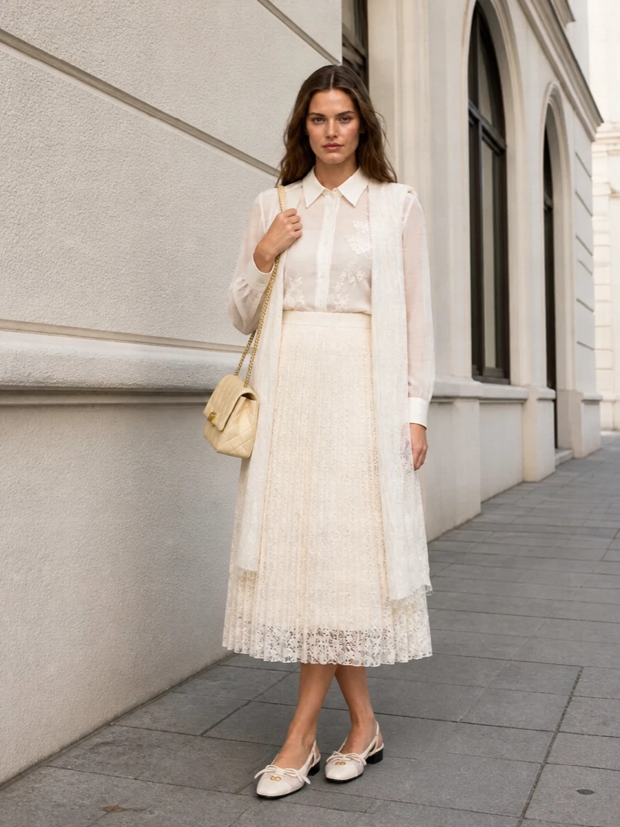 An all-ivory palette of sheer silk and lace creates a soft, romantic ensemble that feels polished yet weightless for warm evenings or daytime occasions. The pleated midi skirt and low-heeled mesh slingbacks keep the proportions elongated but gentle, while the buttercream quilted shoulder bag and gauzy stole add subtle structure and shine without breaking the whisper-light mood. It is an understated, couture-level way to wear neutrals that still feels special and considered from every angle.
