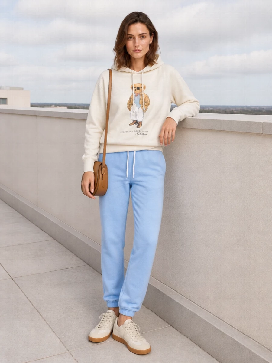 Cream and powder-blue tones keep this Polo Bear hoodie and jogger pairing feeling fresh, collegiate and pulled together for relaxed days. Creamy gum-sole sneakers and a tan saddle bag introduce quiet structure and warmth, grounding the soft palette without breaking the sporty-preppy mood.
