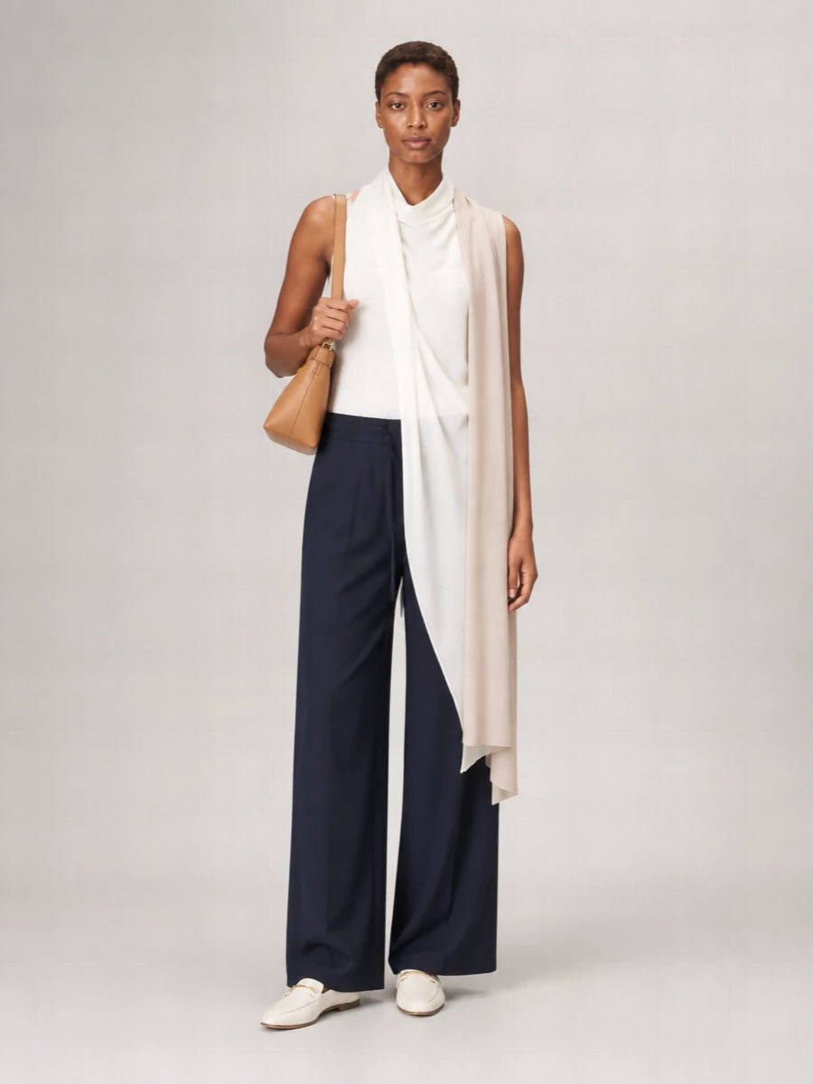 Deep navy wide-leg trousers meet a sculptural soft white sleeveless top for a clean, modern play of volume and drape. Ivory loafers keep the mood relaxed yet precise, while a slim camel shoulder bag and sheer nude scarf quietly warm the palette. The result is an understated, high-summer ensemble that moves easily from gallery afternoons to unhurried dinners.