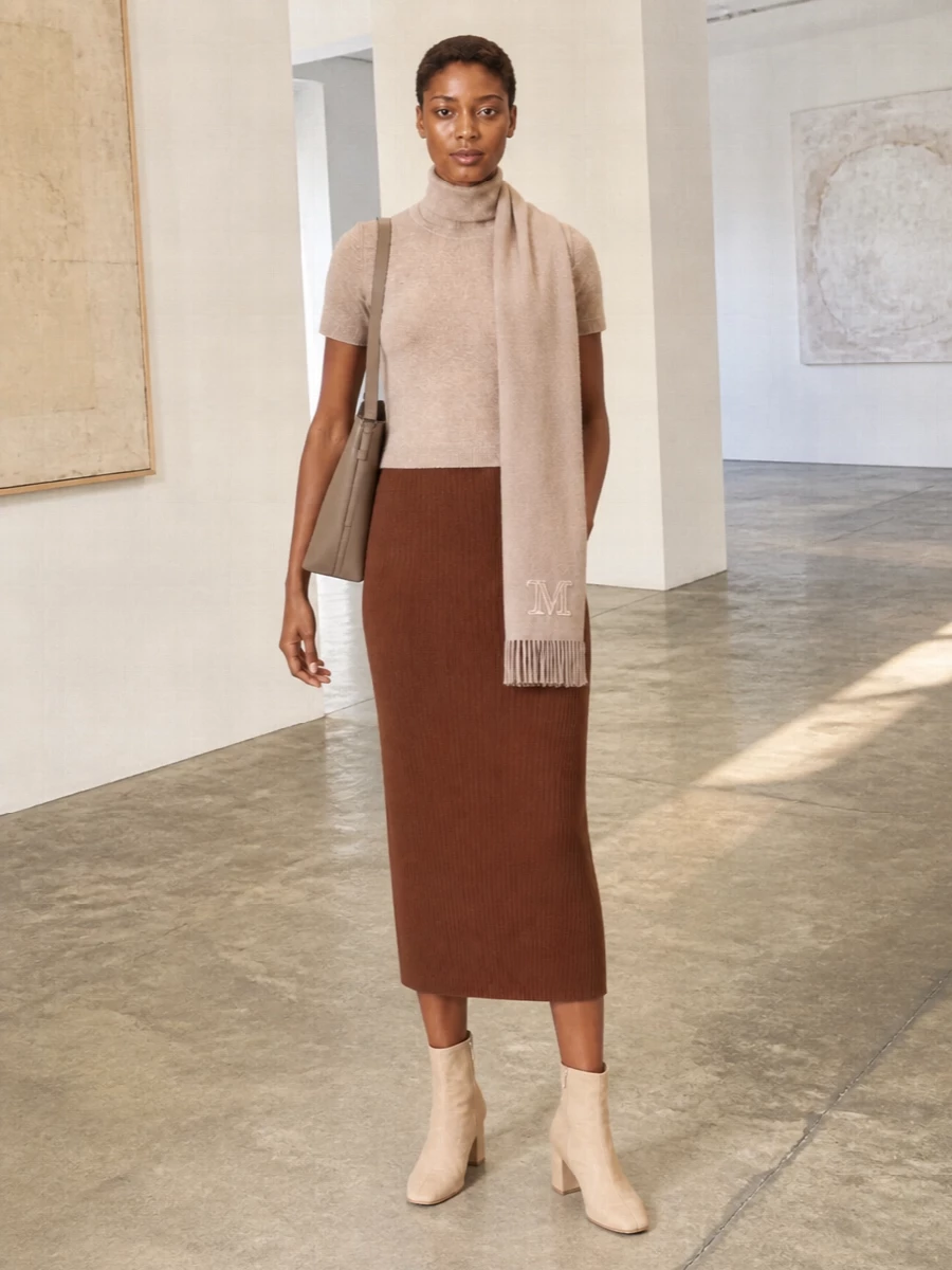 A warm neutral column of knitwear, anchored by the chestnut ribbed skirt and beige turtleneck tee, feels quietly composed and modern. Sand ankle boots and a taupe bucket bag keep the lines elongated while staying within the same calm palette. The softly brushed scarf is the final, tactile layer that adds depth without disturbing the minimalist mood.