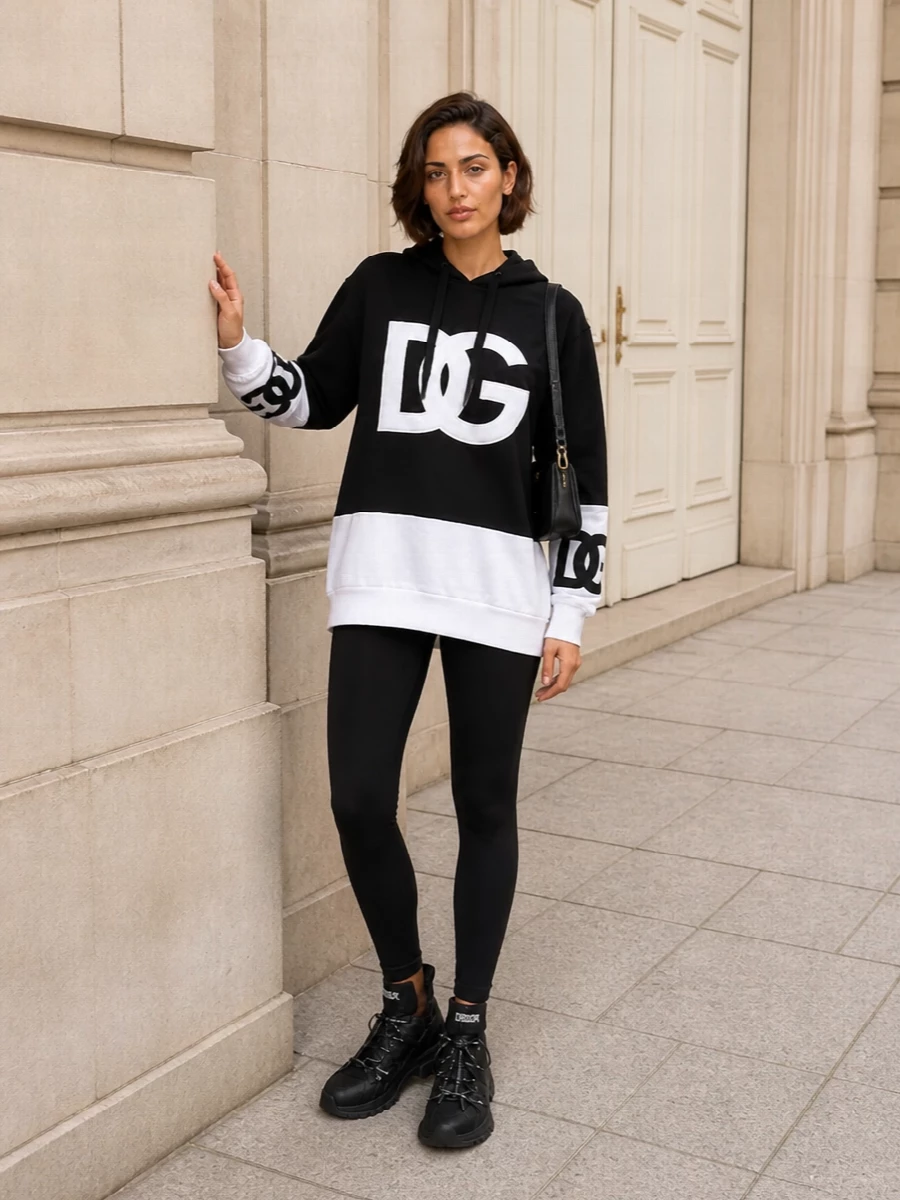 Top and bottom is the right path here, since pairing the logo hoodie with sleek black leggings keeps the focus on Dolce&Gabbana’s bold graphic story instead of competing with a dress silhouette. The result is a monochrome, sport-influenced city ensemble that feels plush, streamlined and distinctly designer from head to toe. Chunky high-top sneakers and a compact black shoulder bag finish it with practical refinement that still reads unapologetically branded.