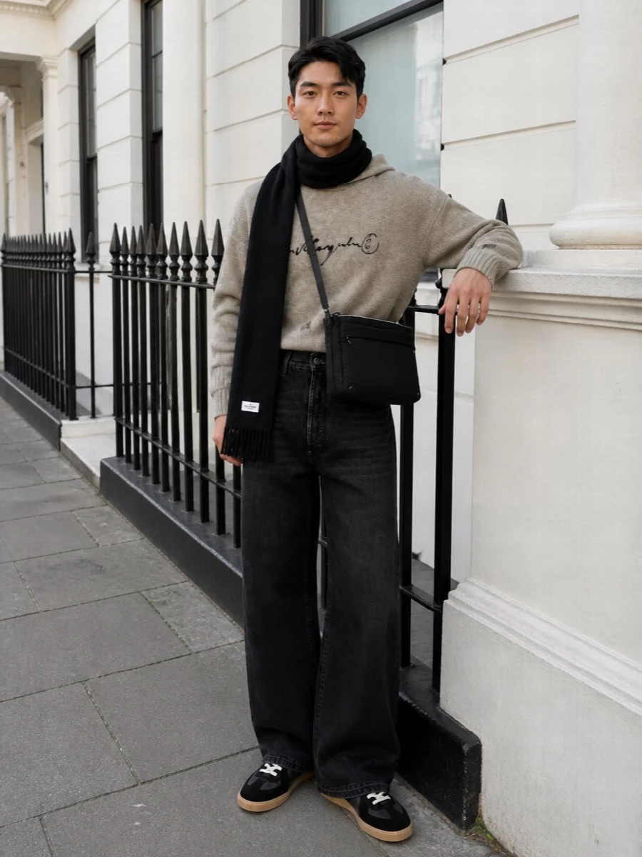 A heather beige Margiela knit hoodie sits over high-waisted washed black wide-leg denim for a relaxed, cocooned silhouette that still feels intentional. Charcoal and black sneakers and a slim quilted crossbody keep the palette tight and urban, while a stark black scarf adds just enough contrast for cold-city days. It is a quietly directional off-duty uniform that reads refined without feeling precious.