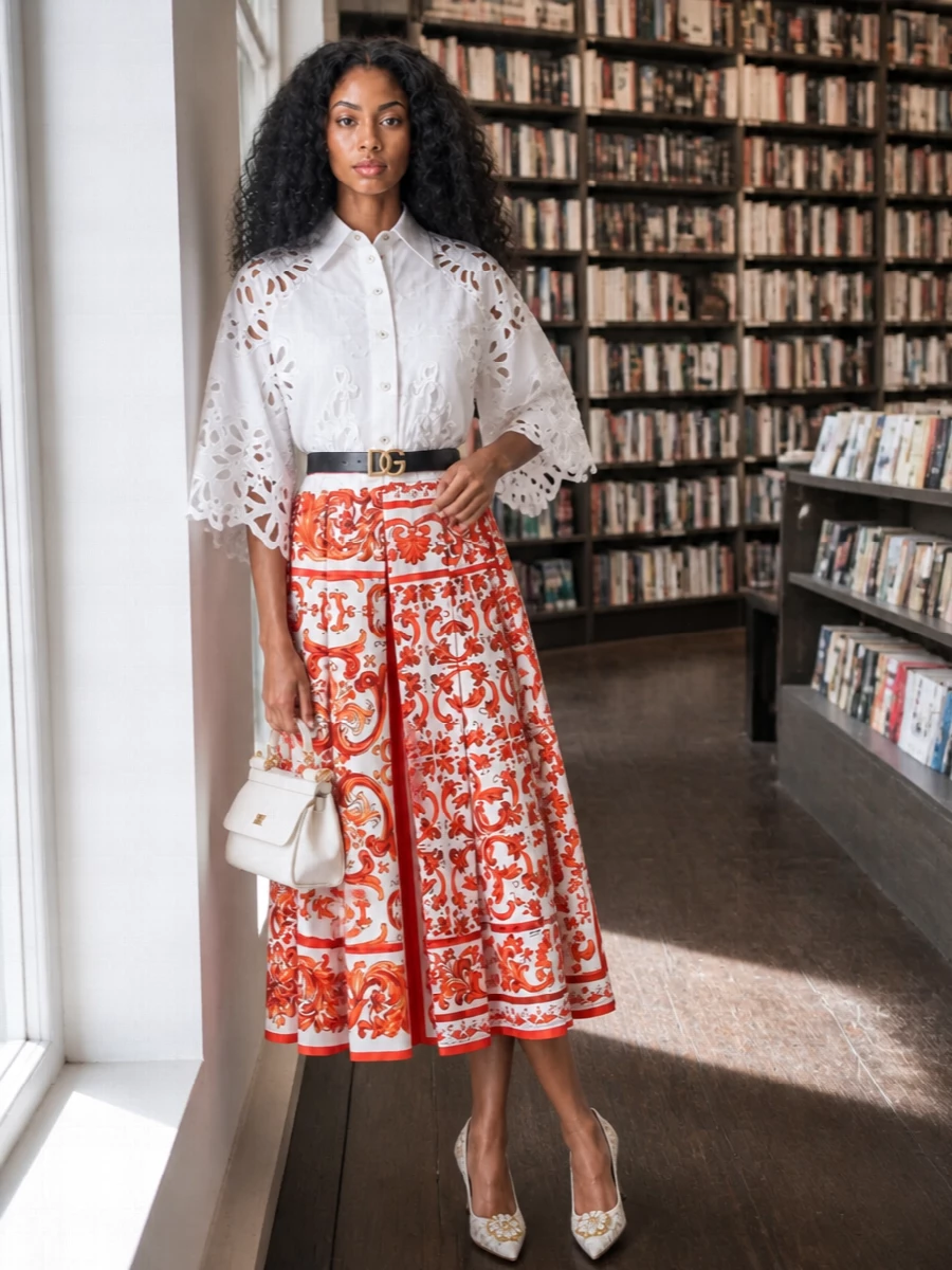 This pairing lets the baroque printed midi skirt lead, grounded by sculptural white cutwork and tonal ivory accessories for a refined romantic mood. A slim logo belt cleanly defines the waist, so the high-rise pleats read sharp rather than busy. It is polished enough for city dinners or garden parties while still feeling light and Mediterranean-leaning in spirit.