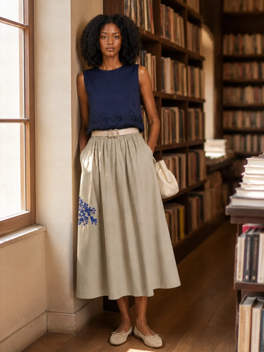 Sand and navy play softly together, with embroidered florals linking top and skirt into a quiet summer story. Neutral flats and a creamy sculpted bag keep the mood light and relaxed, while a slim blush belt adds just enough definition at the waist. It is an easy city-to-coast outfit that feels considered without trying too hard.