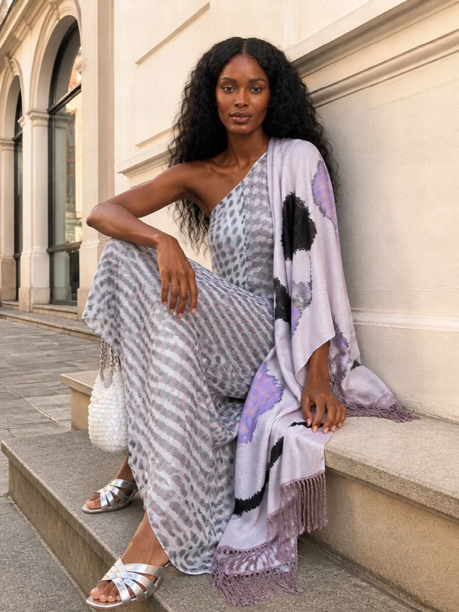 A gauzy Dries maxi does the talking, its one‑shoulder drape and polka dots setting a romantic, art‑world mood. Silver mules and a pearl‑sequin clutch catch just enough light, while a lilac‑toned scarf ties the palette together for warm‑night cocktails. The result feels soft, sculptural and quietly dramatic without tipping into costume.
