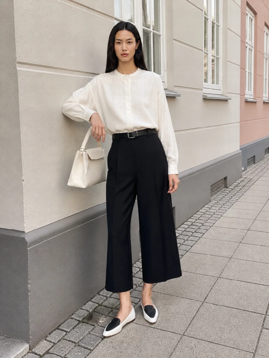 A soft ivory shirt and deep navy-black cropped wide leg create a quiet yet graphic column of colour. The pointed flat loafer refines the volume at the hem, while a structured ivory top-handle and slim black belt keep the whole composition clean and assured for modern city days.