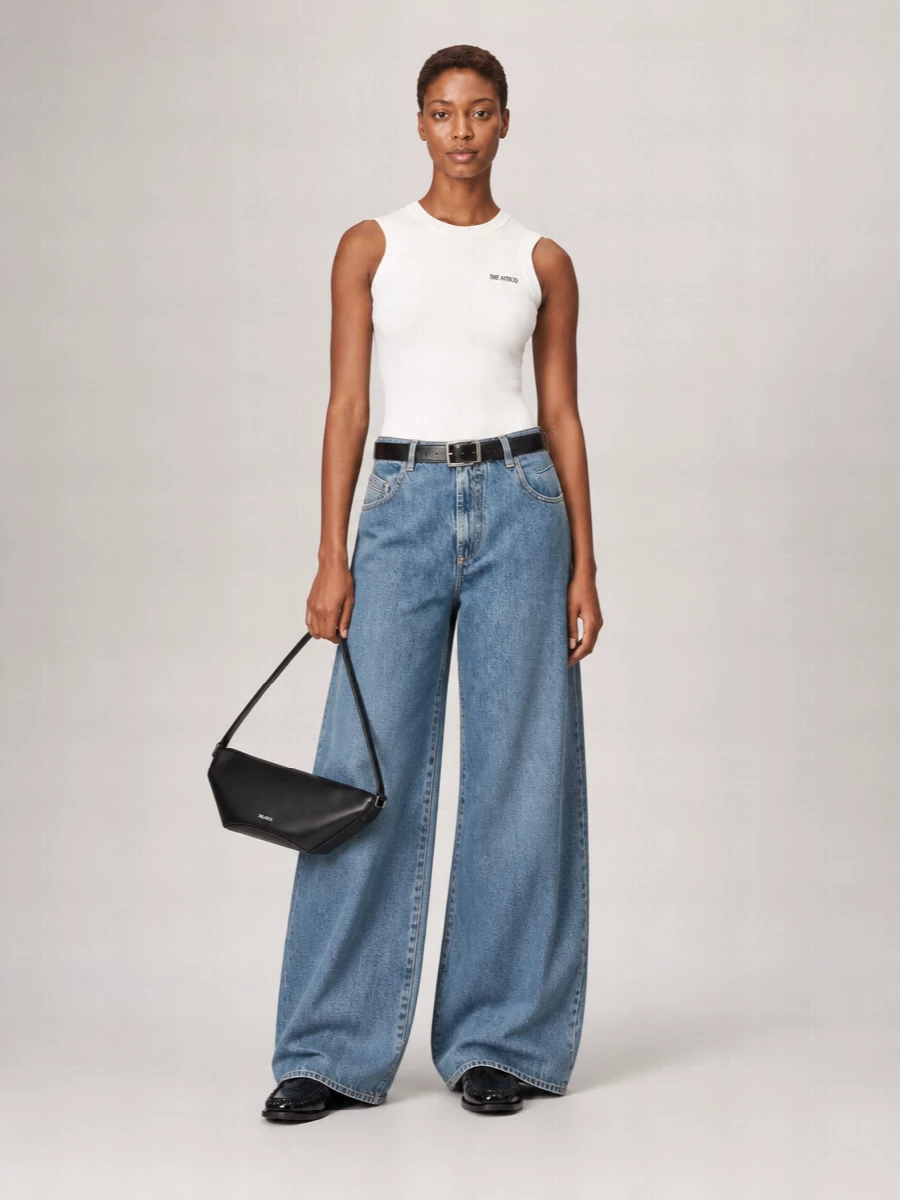 A soft-white logo tank meets exaggerated mid-wash wide-leg denim for a clean, street-aware base that still feels quietly refined. Glossy black loafers and a sharp Attico baguette pull the palette back to monochrome, while a slim logo belt cinches the volume just enough. Perfect when you want a relaxed jean silhouette that still reads considered and city-ready.