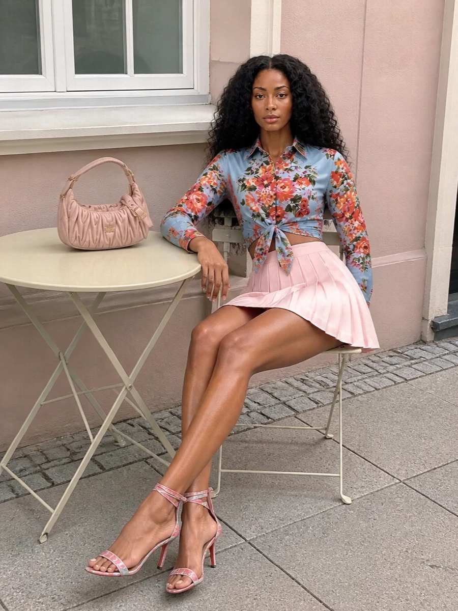 Dolce&Gabbana’s floral tie-front shirt and the blush Thom Browne pleated mini create a fresh, romantic silhouette that nods to prep without losing softness. The floral Louboutin sandals pick up the shirt’s sky blue and poppy tones, while the ruched Miu Miu bag keeps the palette light and feminine for terrace lunches or garden parties. High-waisted volume under the cropped knot keeps everything balanced and flattering from every angle.