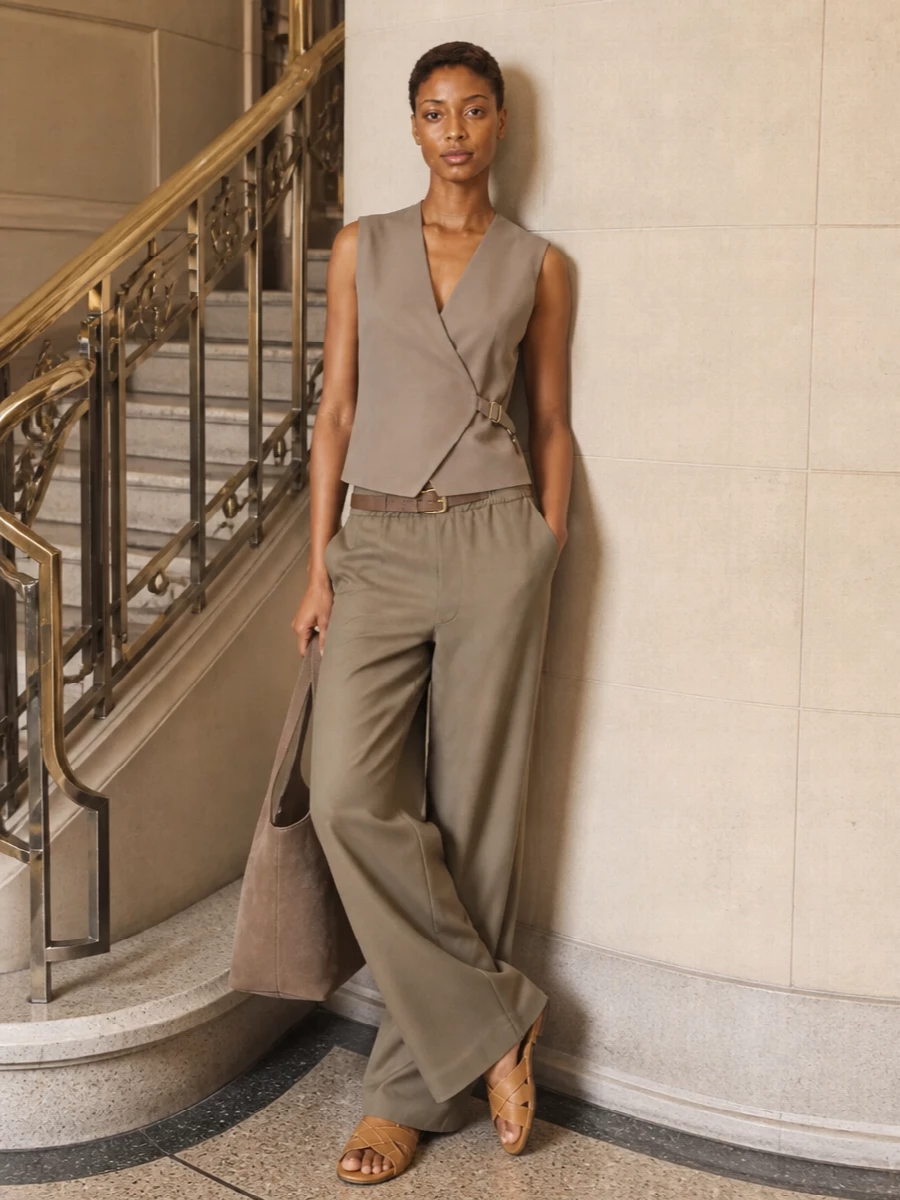 A column of warm taupe and tan feels calm and precise, with the wrap vest neatly framing the waist above the fluid wide leg. Flat leather slides keep it grounded and easy, while a soft suede tote and slim belt add just enough texture for understated daytime polish. Ideal for warm days when you want to feel relaxed but considered.