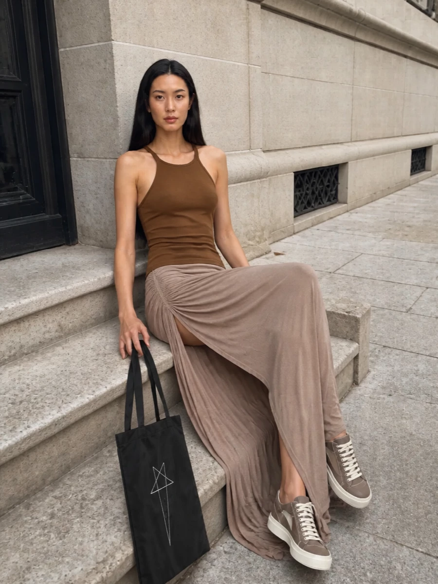 This look leans into Rick’s elongated, SS-ready column: the chocolate tank and taupe ruched maxi skirt create a fluid, tonal line that feels subversive yet minimal. Taupe platform low-tops ground the silhouette with a graphic street edge, while the flat black tote adds a stark, urban note without breaking the palette or the proportions. It’s an easy day-to-night uniform that stays sharp, directional and fully DRKSHDW in attitude.
