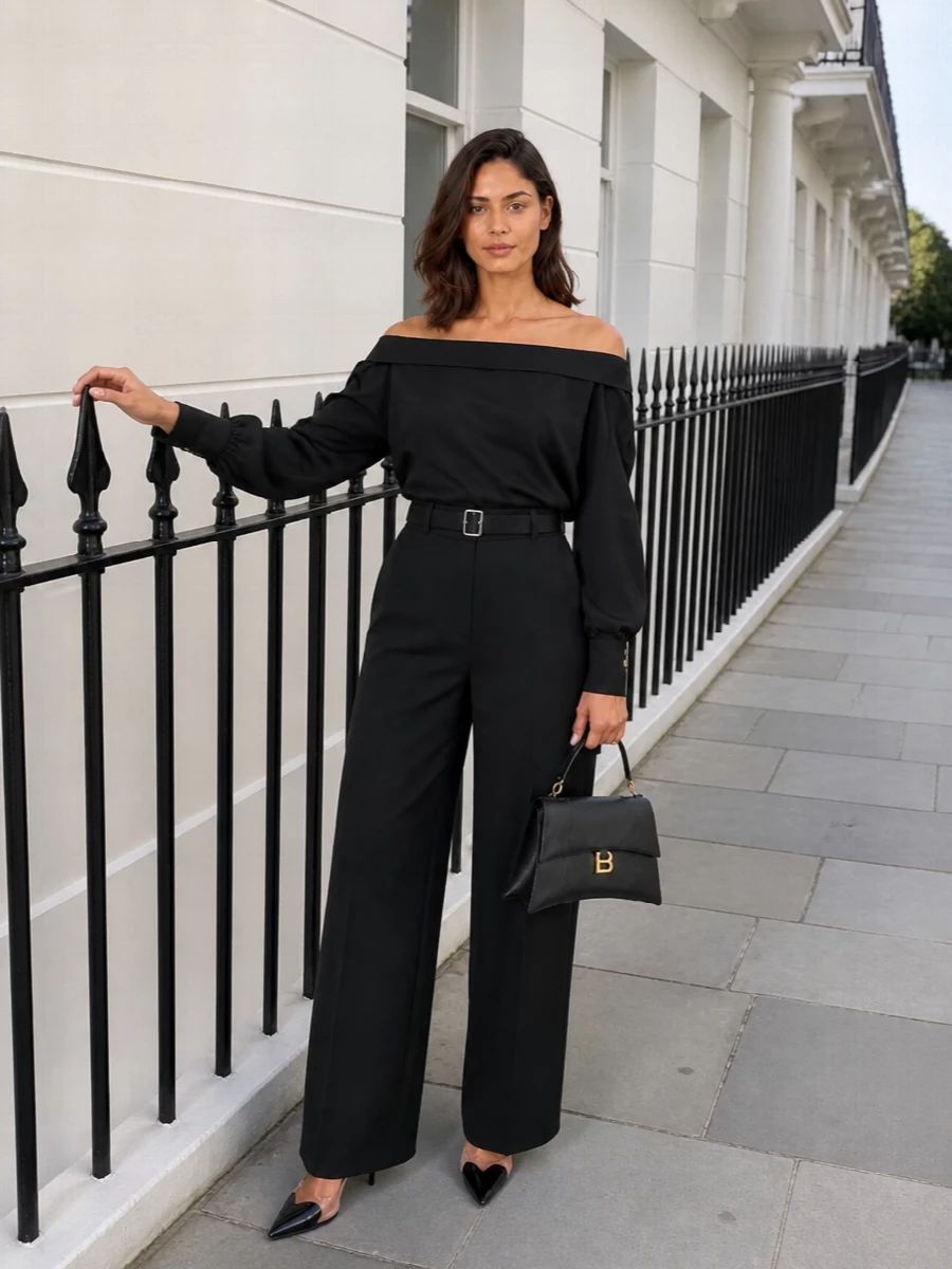 A monochrome evening ensemble that plays with line and exposure, the high waisted wide leg anchors a sculpted off the shoulder top and knife point slingbacks. Silver hardware and clean black leather keep the mood precise and pared back, while a structured top handle bag adds just enough architectural polish for gallery nights and formal dinners alike.