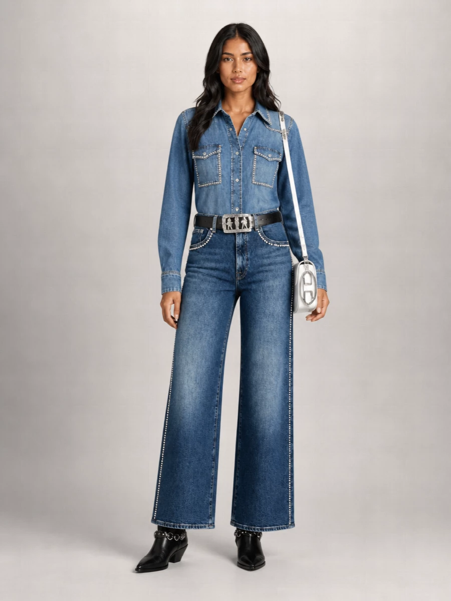 Crystal-trimmed denim on top and bottom leans fully into a polished Western mood, with the high-waist wide leg balancing the longline shirt for a clean, elongated line. Black cowboy boots and a sculptural belt ground the blue-on-blue with structure, while a sharp white cross-body in silver-trimmed leather brings a graphic Y2K hit without competing with the studs.