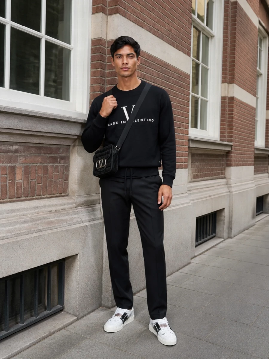 Graphic monochrome Valentino sneakers sit under a black logo sweatshirt, anchored by tailored drawstring trousers for a clean, modern line. The result is relaxed city dressing with couture-level detailing and a sharp streetwear edge. A compact monogram crossbody keeps the focus on proportion and branding without adding bulk.