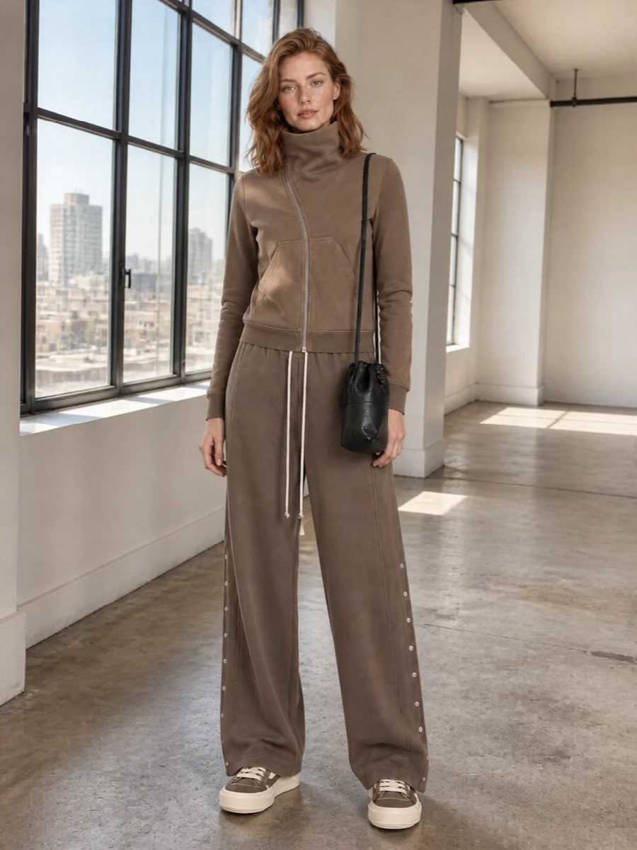 Taupe-on-taupe DRKSHDW—the funnel-neck sweatshirt and washed wide-leg trouser in matching tones create a relaxed column that feels cocooned yet sharp. Chunky taupe platform sneakers keep the line grounded and directional, while the slim black crossbody adds just enough structure and attitude without disturbing the minimalist, street-leaning mood. It’s an easy, off-duty uniform that still reads distinctly Rick from every angle.