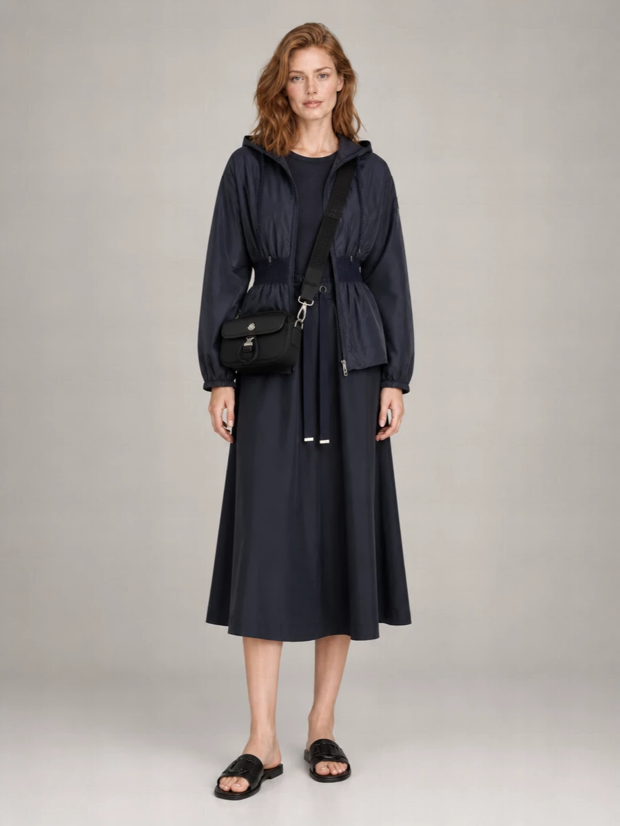 I am building around the outerwear plus dress path, letting the navy parka sit over a fluid navy midi for a clean sport-luxe column. The technical dress keeps the silhouette long and sleek under the cinched waist, while pared-back black slides and a compact nylon cross-body keep everything agile enough for city days without breaking the minimalist navy-and-black story. The result feels like a modern travel uniform that reads polished but still very practical and easy to move in.