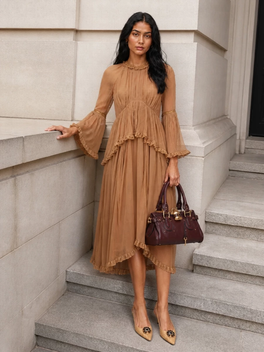 I chose the dress route so the Zimmermann caramel chiffon can carry the romance, letting the Chloé satchel read as a rich accent rather than compete with separates. The tiered midi and soft fluted sleeves create an ethereal swish, grounded by the structured burgundy bag for day-to-dinner polish. Valentino’s caramel slingbacks keep the palette warm and cohesive, so the whole outfit feels bohemian yet quietly refined for autumn evenings or long lunches.