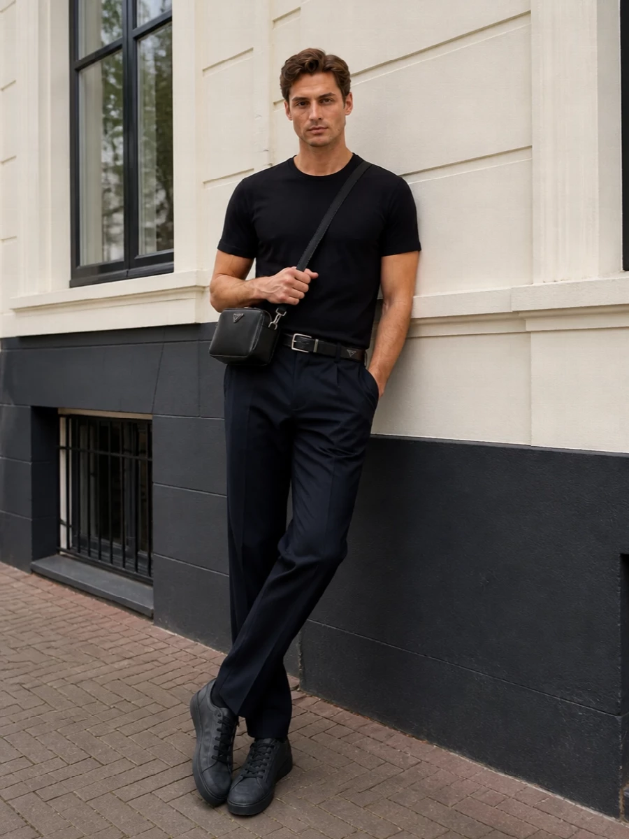 A black Herno tee and tailored navy trousers create a quiet, low-contrast base that feels considered without reading formal. Charcoal Tod’s sneakers keep everything grounded yet relaxed, while a structured black Prada crossbody and belt sharpen the line for city days that move easily into dinner. The result is a dark, tonal uniform that feels precise, comfortable and deliberately understated.