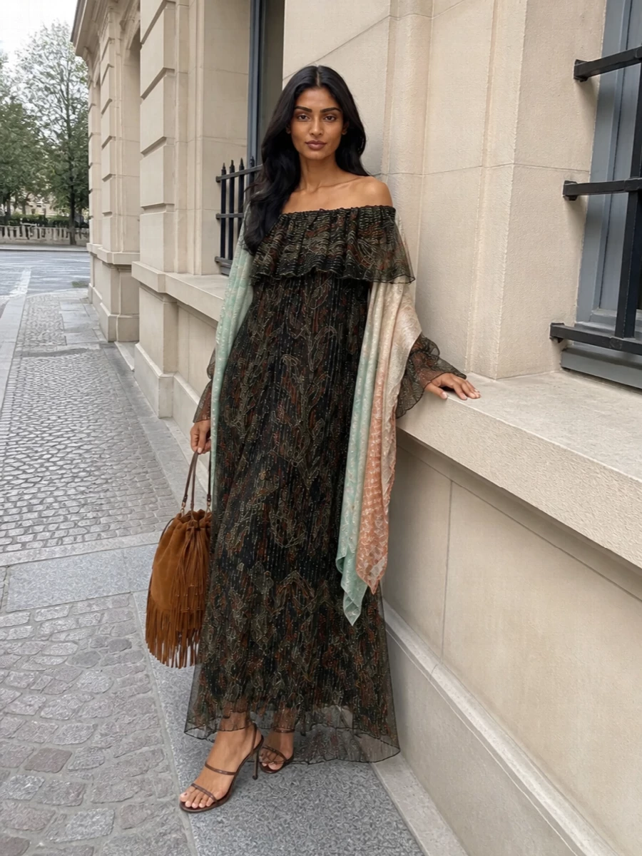Saint Laurent’s off-shoulder paisley maxi takes the lead, its sheer chiffon and metallic threads playing against the rich depth of black and rust. Barely-there chocolate sandals keep the line elongated and sensual, while the tan suede fringe bag adds a soft, tactile boho note that moves with the dress. The result is a romantic evening ensemble with an easy, luminous sway rather than hard polish.