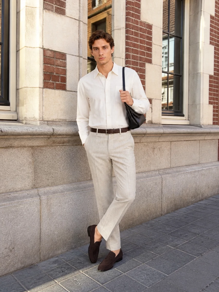 A crisp white shirt sits over light beige tailoring for a clean, modern take on smart city dressing. Dark brown suede loafers and a matching belt bring depth without breaking the calm palette, while a slim black shoulder bag adds just enough structure for a work-to-dinner day. The result is quietly refined and easy to wear, with proportions that feel precise rather than fussy.